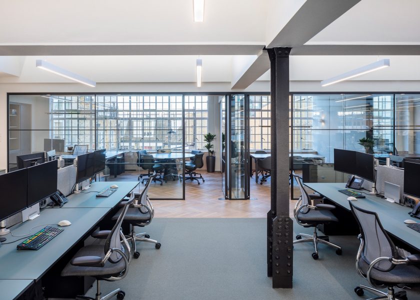 Open plan work-space decorated with wood floor tiles and multiple meeting rooms divided by glazed glass partitions.