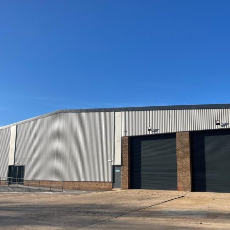 Industrial warehouse facade with grey cladding and shutter doors on a dunny day.